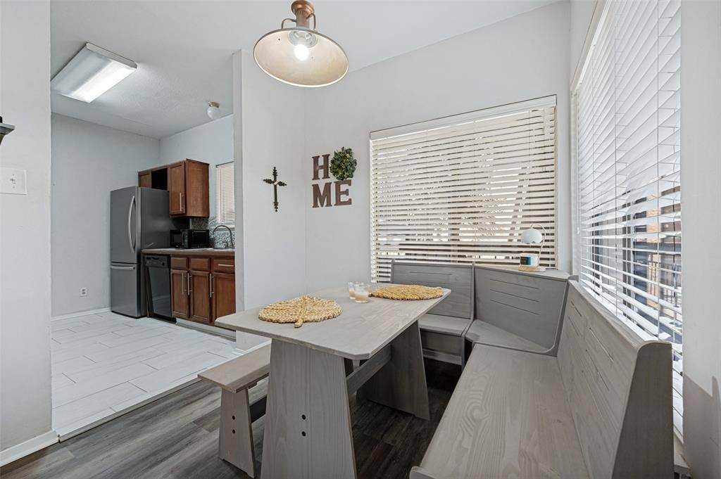5550 Spring Valley Road, #C21, Dallas, TX 75254 Built-in dining bench seating, wood-finish flooring, overhead lighting, and kitchen area with stainless steel refrigerator and dark wood cabinetry