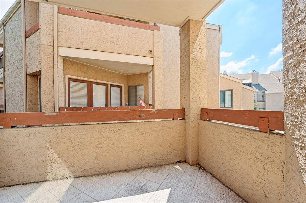 5550 Spring Valley Road, #C21, Dallas, TX 75254 Exterior balcony featuring textured stucco walls, a wood-finished railing, and patterned tile flooring