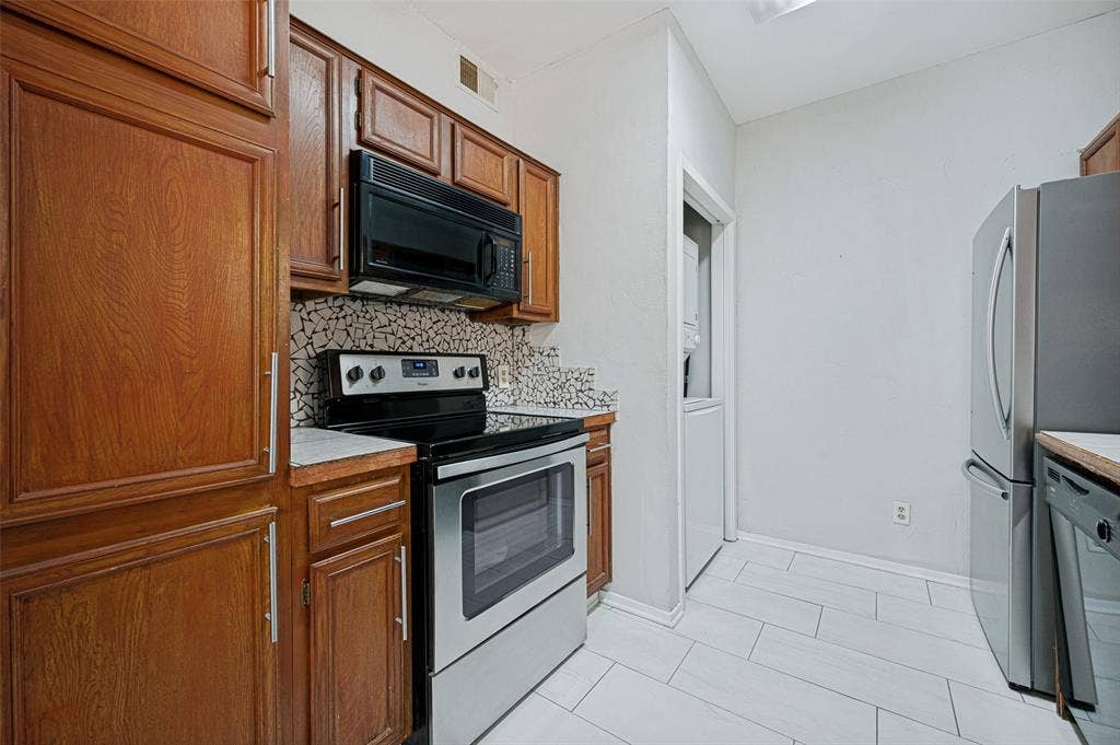 5550 Spring Valley Road, #C21, Dallas, TX 75254 Wood cabinetry, mosaic tile backsplash, black over-the-range microwave, stainless steel range, and light-toned tile flooring