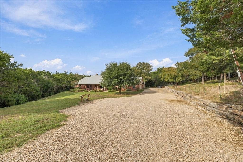 1600 Fox Ridge Road, Lorena, TX 76655 Expansive property featuring a gravel driveway, natural stone retaining wall, mature trees, and a covered front porch