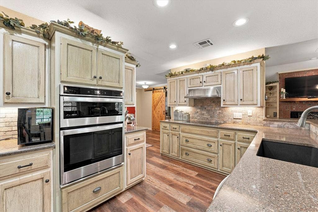 1600 Fox Ridge Road, Lorena, TX 76655 Kitchen featuring wood cabinetry with a distressed finish, stone-tiled backsplash, stainless steel double wall ovens, wood-finish flooring, and recessed lighting