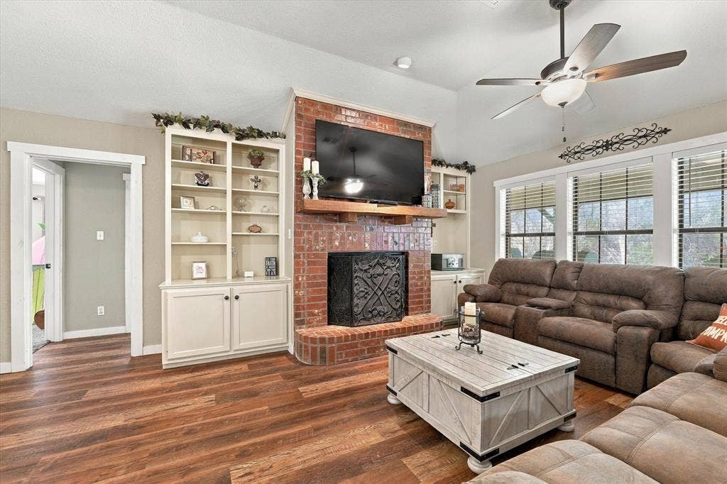 1600 Fox Ridge Road, Lorena, TX 76655 Vaulted ceiling with a central paddle fan, floor-to-ceiling brick fireplace with a custom wood mantel, and custom white built-in cabinetry featuring shelving and lower storage