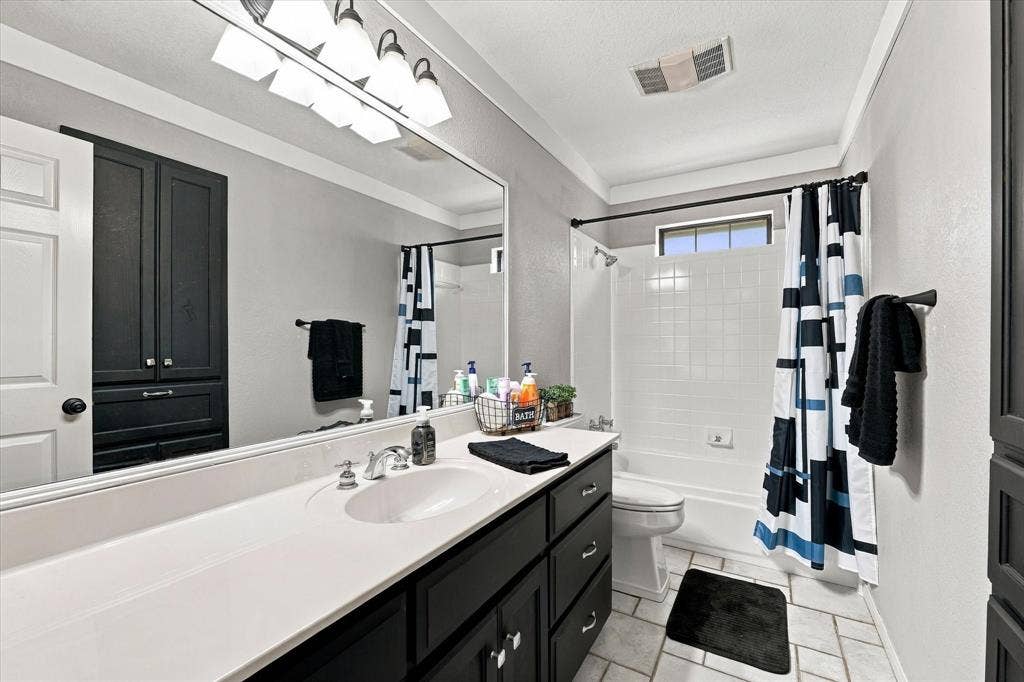 1600 Fox Ridge Road, Lorena, TX 76655 Bathroom featuring a dark-finish vanity with a light countertop, integrated sink, full-width mirror with four-light fixture, and a tiled tub-shower combination