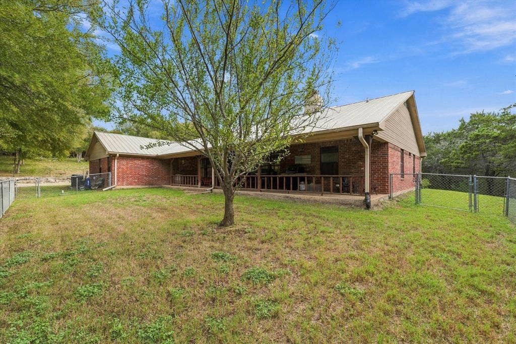 1600 Fox Ridge Road, Lorena, TX 76655 Red brick exterior featuring a metal roof, expansive covered porch with railing, and a fenced backyard