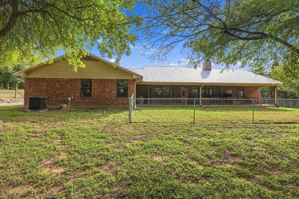 1600 Fox Ridge Road, Lorena, TX 76655 Single-story brick exterior featuring a metal roof, rear covered porch, chain-link fencing, and mature trees
