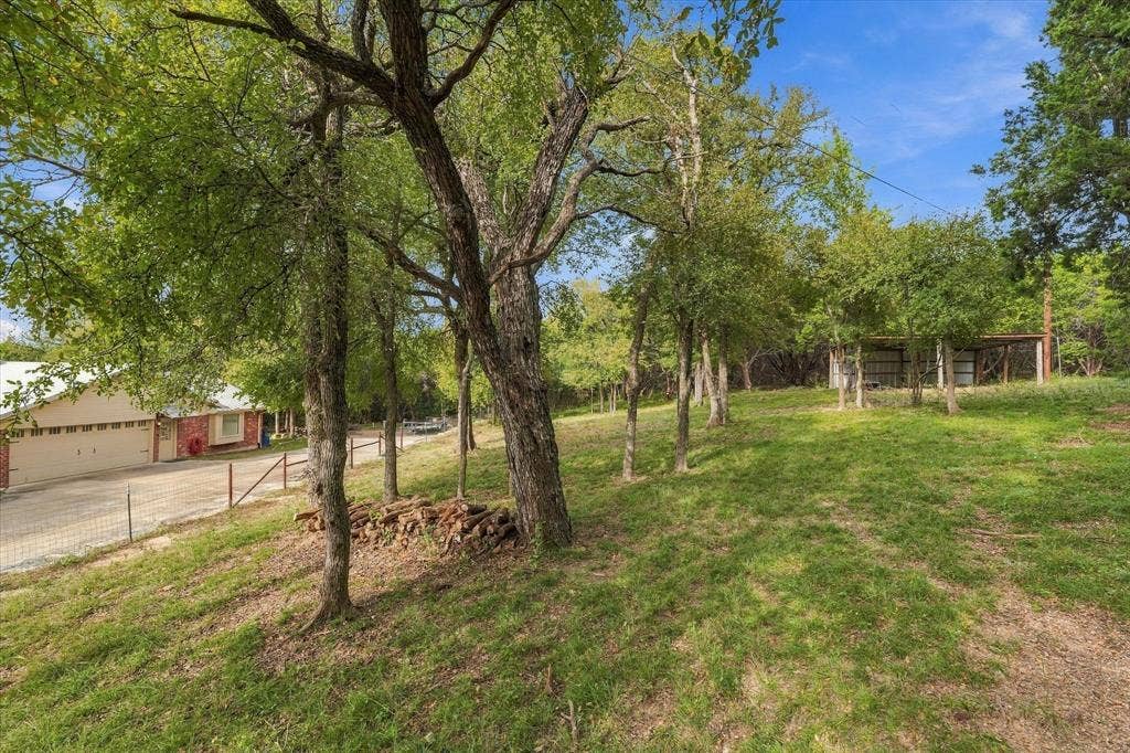 1600 Fox Ridge Road, Lorena, TX 76655 Expansive lot featuring mature trees, a concrete driveway, multi-car garage, and an open-air detached storage structure