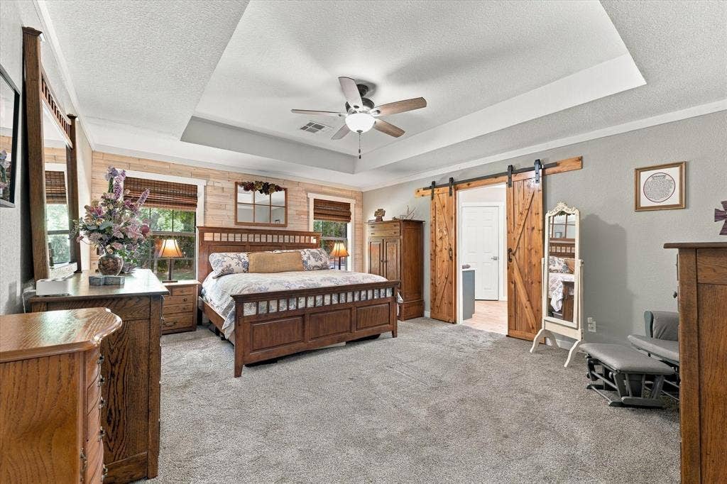 1600 Fox Ridge Road, Lorena, TX 76655 Tray ceiling with central light fixture and ceiling fan, wood-plank accent wall, and sliding wood barn door