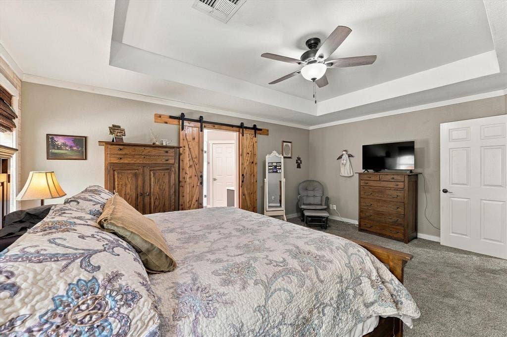 1600 Fox Ridge Road, Lorena, TX 76655 Tray ceiling with crown molding, ceiling fan with light kit, sliding barn door with exposed hardware, and multi-panel interior door
