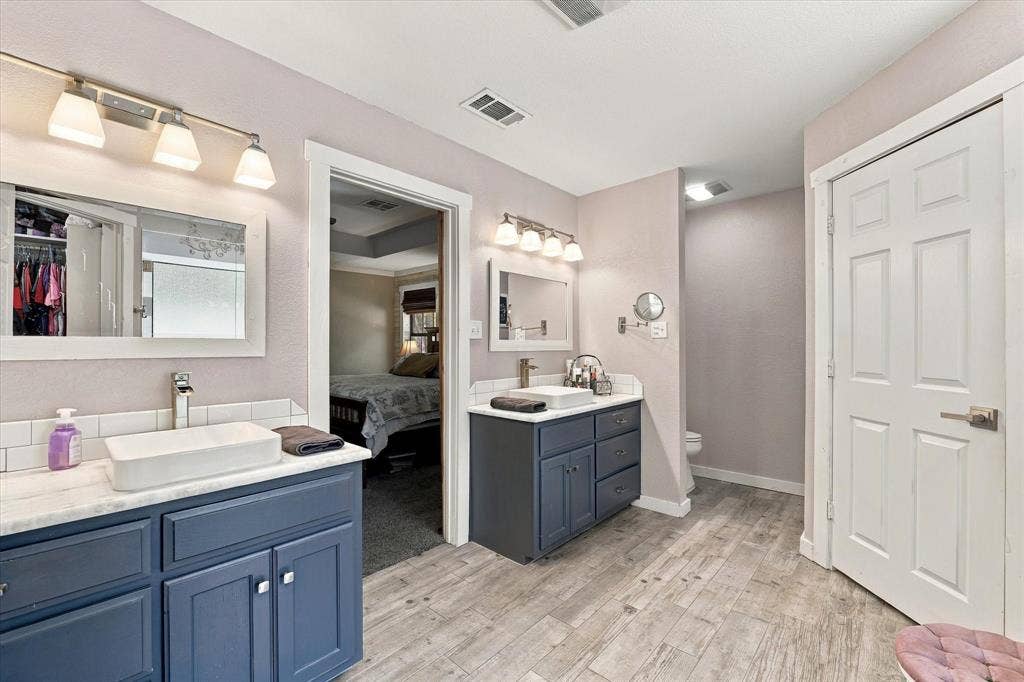1600 Fox Ridge Road, Lorena, TX 76655 Dual vanity featuring navy blue cabinetry, rectangular vessel sinks, stone-finish countertops, and wood-finish flooring