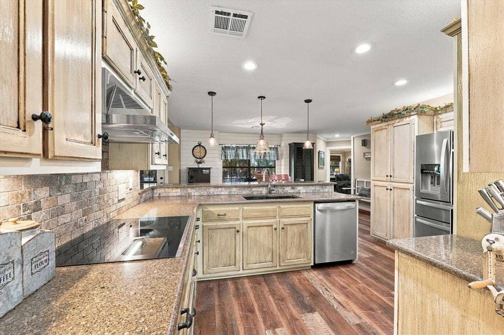 1600 Fox Ridge Road, Lorena, TX 76655 Kitchen featuring wood-finish flooring, stone-tiled backsplash, stainless steel appliances, built-in cabinetry, and pendant lighting