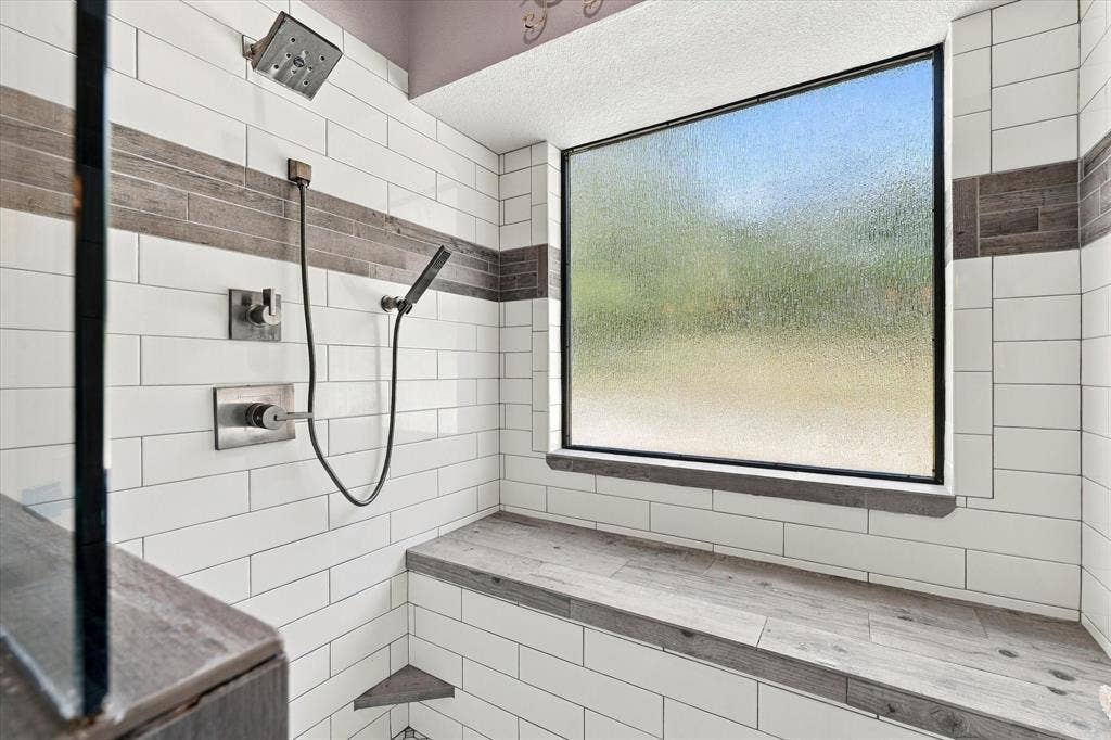 1600 Fox Ridge Road, Lorena, TX 76655 Walk-in shower featuring subway tile walls, wood-finish tile accent banding, built-in bench seating, a rain shower head with a handheld sprayer, and an integrated window with frosted glass