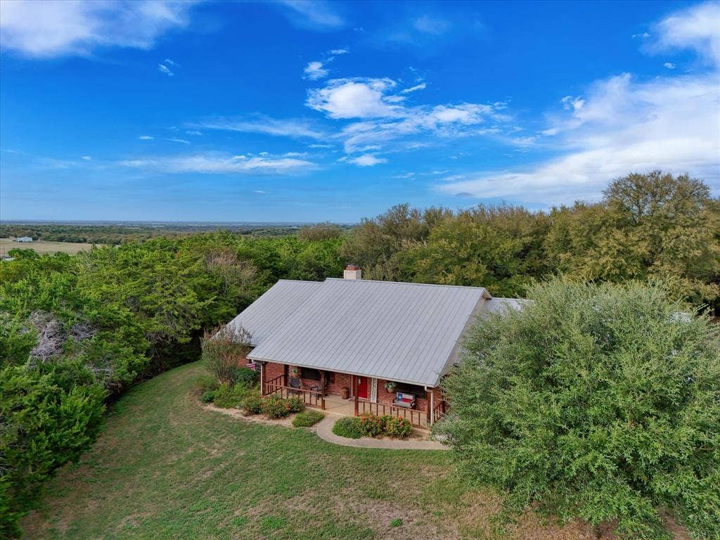 1600 Fox Ridge Road, Lorena, TX 76655 Single-story residence featuring a metal roof, brick exterior, covered front porch, and expansive acreage with mature trees