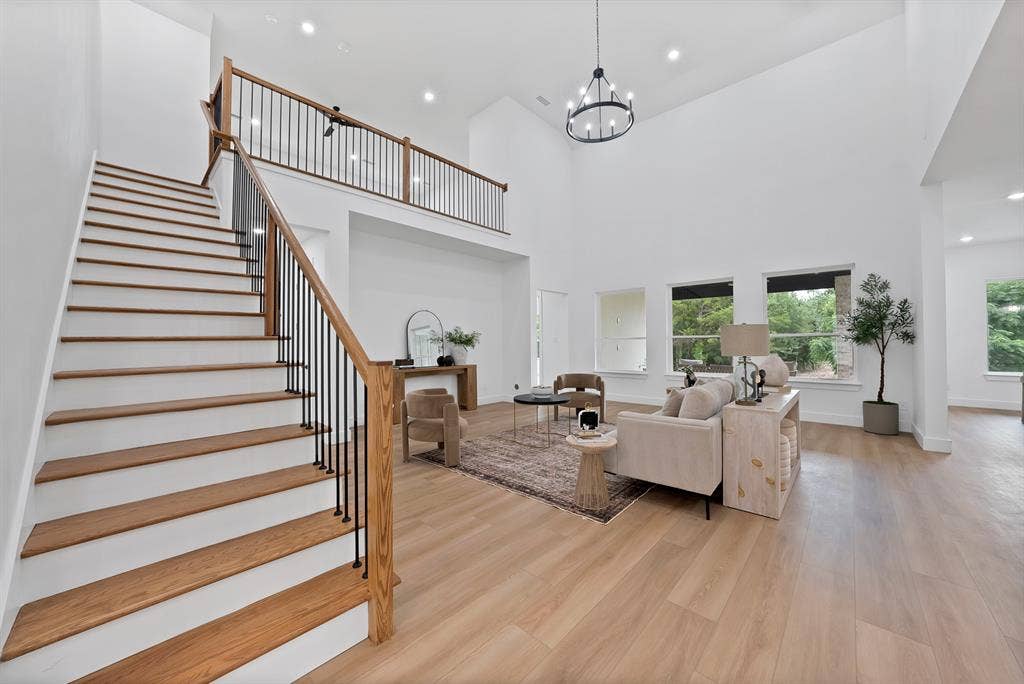 Two-story living area with high ceilings, wood-finish flooring, and an open staircase with a wood handrail and black metal spindles