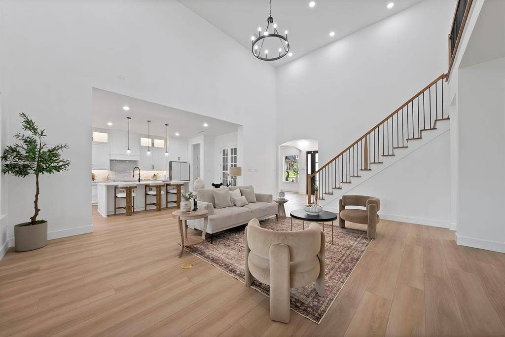 Two-story living area with wood-finish flooring, a contemporary chandelier, and recessed lighting