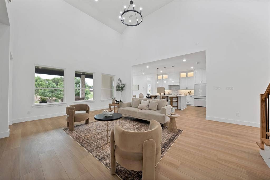 Vaulted ceiling with a contemporary chandelier, light wood-finish flooring, and multiple windows