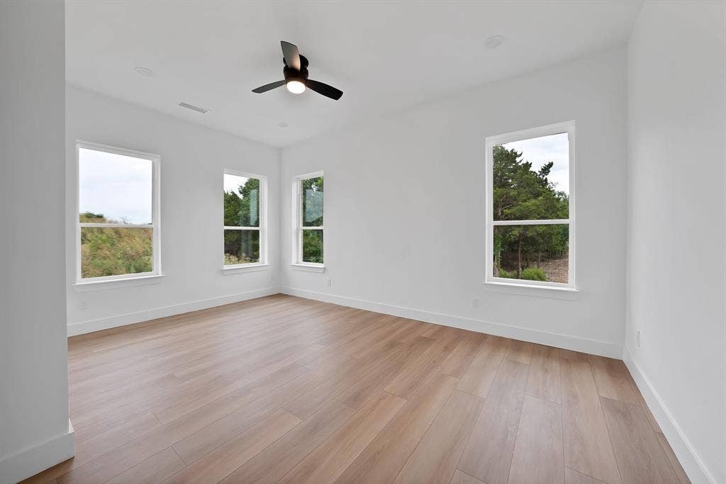 Bright room featuring wood-finish flooring, white walls, multiple windows, and a ceiling fan with integrated lighting