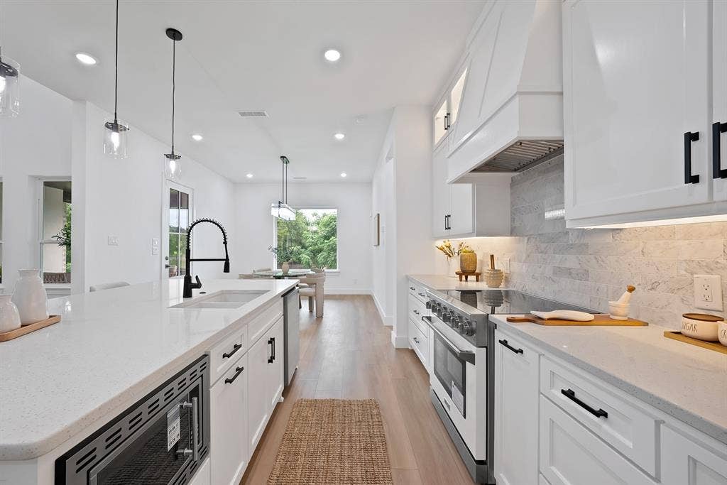 White cabinetry with black hardware, stone countertops, wood-finish flooring, undermount sink with a matte black faucet, and recessed and pendant lighting