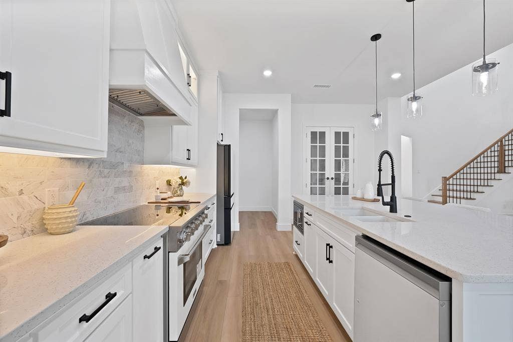 White shaker cabinetry with matte black hardware, stone countertops, stainless steel range with hood, and a built-in kitchen island with sink and pendant lighting
