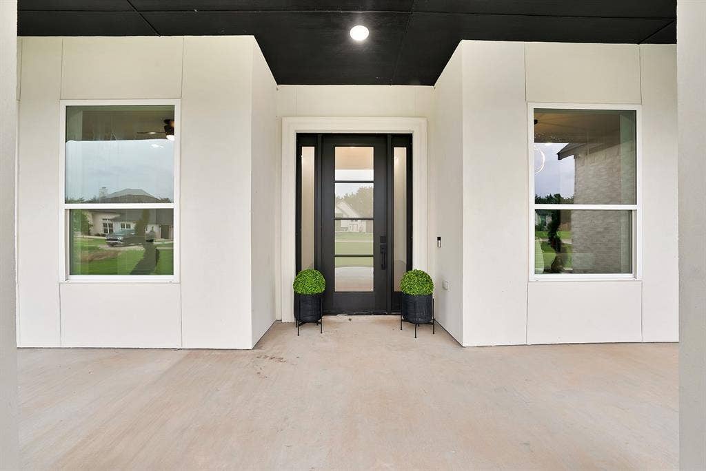 Covered front porch with a dark ceiling accent, vertical white paneling, and a full-light entry door