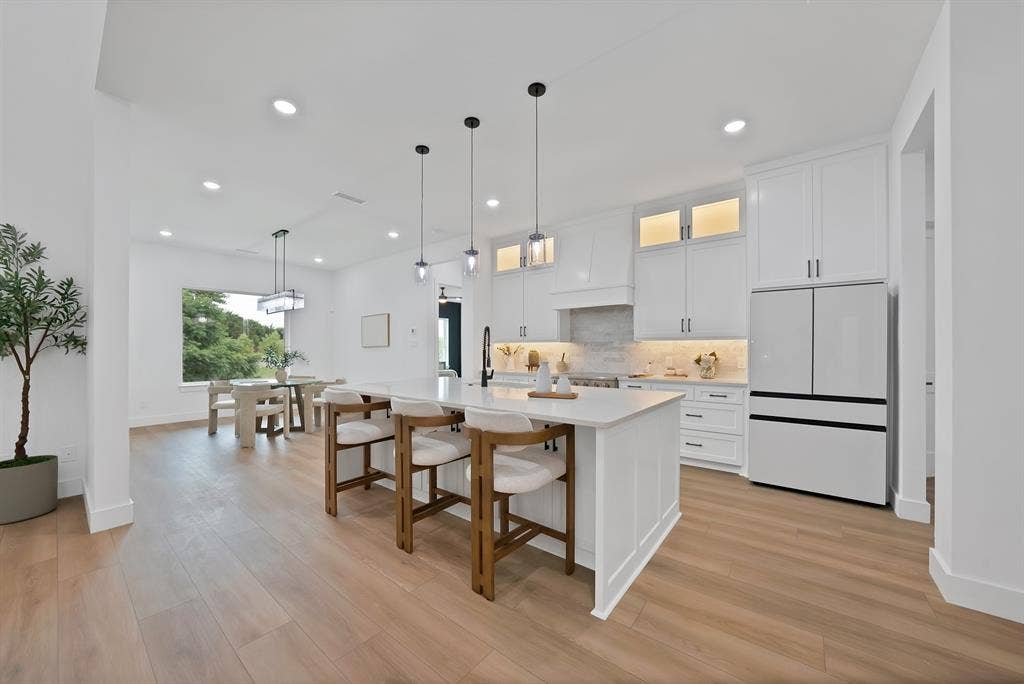 Kitchen featuring a large central island, white cabinetry, integrated appliances, wood-finish flooring, and recessed lighting