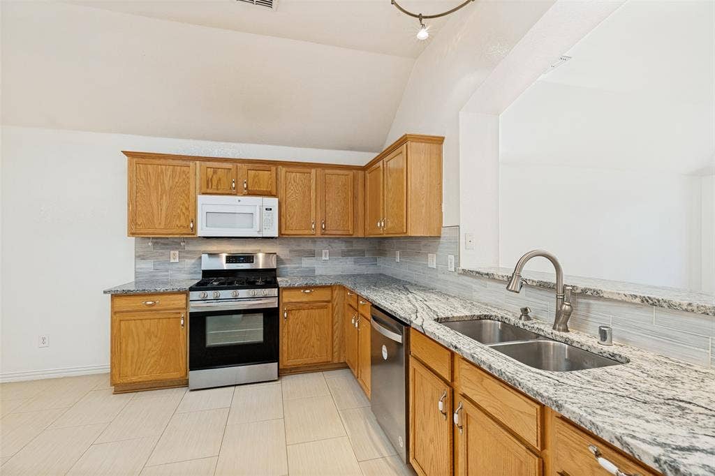 1412 Sleepy Hollow Drive, Allen, TX 75002 Kitchen featuring a vaulted ceiling, wood-finish cabinetry, stainless steel appliances, granite countertops, and a double basin sink