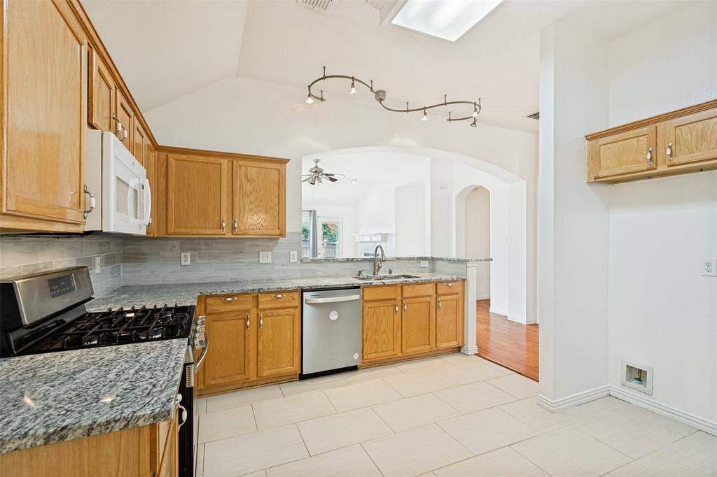 1412 Sleepy Hollow Drive, Allen, TX 75002 Kitchen featuring light wood cabinetry, white tile flooring, stainless steel appliances, and a skylight