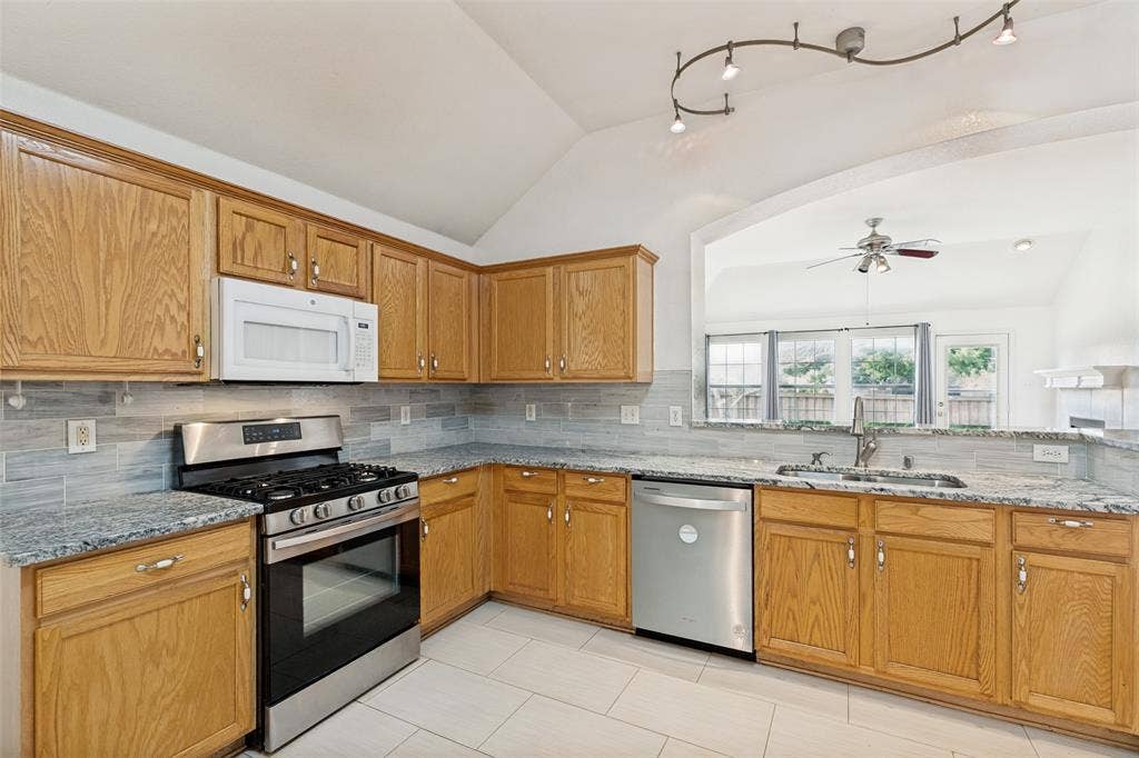 1412 Sleepy Hollow Drive, Allen, TX 75002 Kitchen with wood cabinetry, stainless steel appliances, granite-style countertops, and a gray subway tile backsplash
