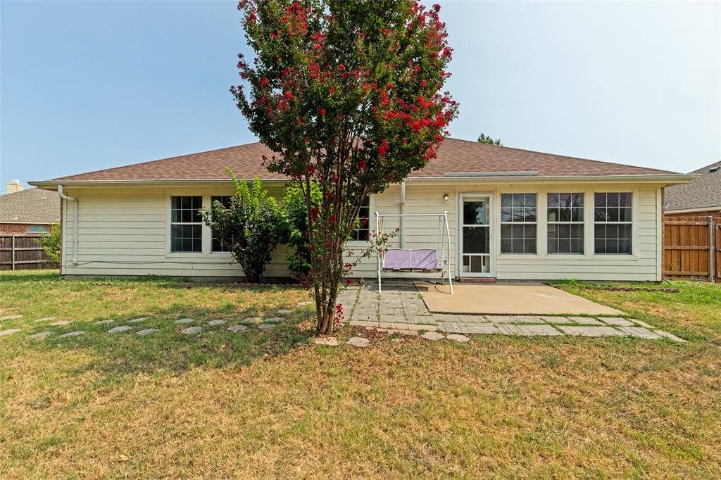 1412 Sleepy Hollow Drive, Allen, TX 75002 Rear exterior with light-colored siding, a brown shingled roof, a paved patio, and a mature tree with red blossoms