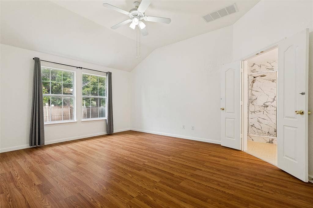 1412 Sleepy Hollow Drive, Allen, TX 75002 Vaulted ceiling with a ceiling fan, dual windows, wood-finish flooring, and an open doorway to a shower with white and gray veined tile