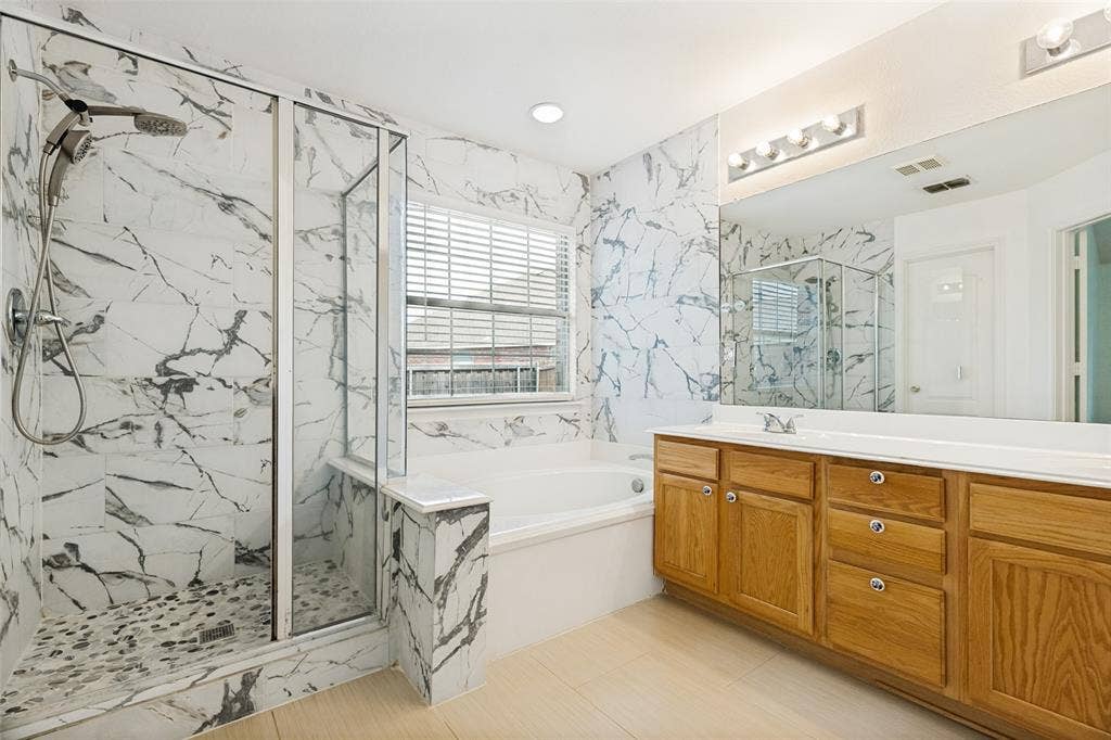 1412 Sleepy Hollow Drive, Allen, TX 75002 Enclosed glass shower with pebble-finish flooring, white tiled walls, a separate soaking tub, and a double vanity with wood cabinetry