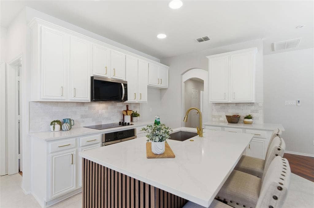 1416 Sunrise Lane, Sachse, TX 75048 White cabinetry, stainless steel microwave, integrated cooktop, island with solid surface countertop, and undermount sink with gold-finish faucet