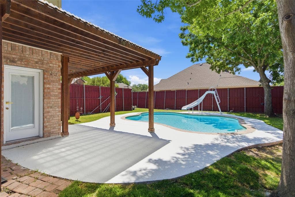 1416 Sunrise Lane, Sachse, TX 75048 Brick exterior with a covered patio, freeform swimming pool, and a private perimeter fence
