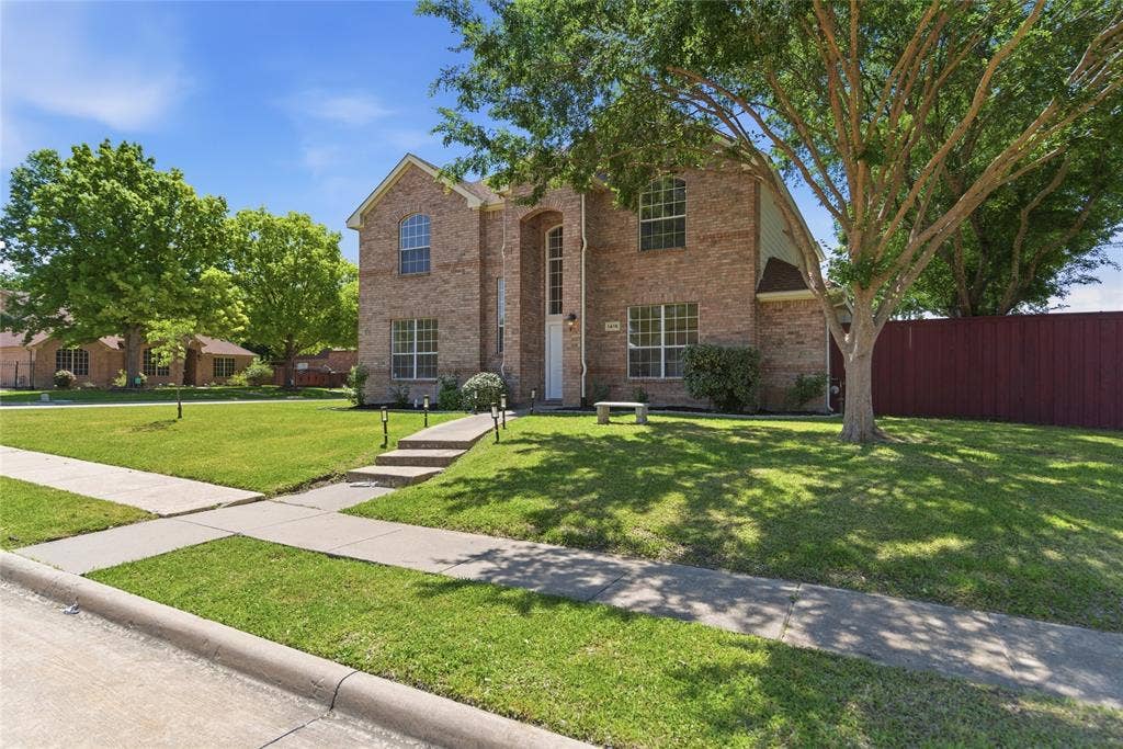 1416 Sunrise Lane, Sachse, TX 75048 Brick exterior with arched windows, manicured lawn, established trees, and concrete walkways