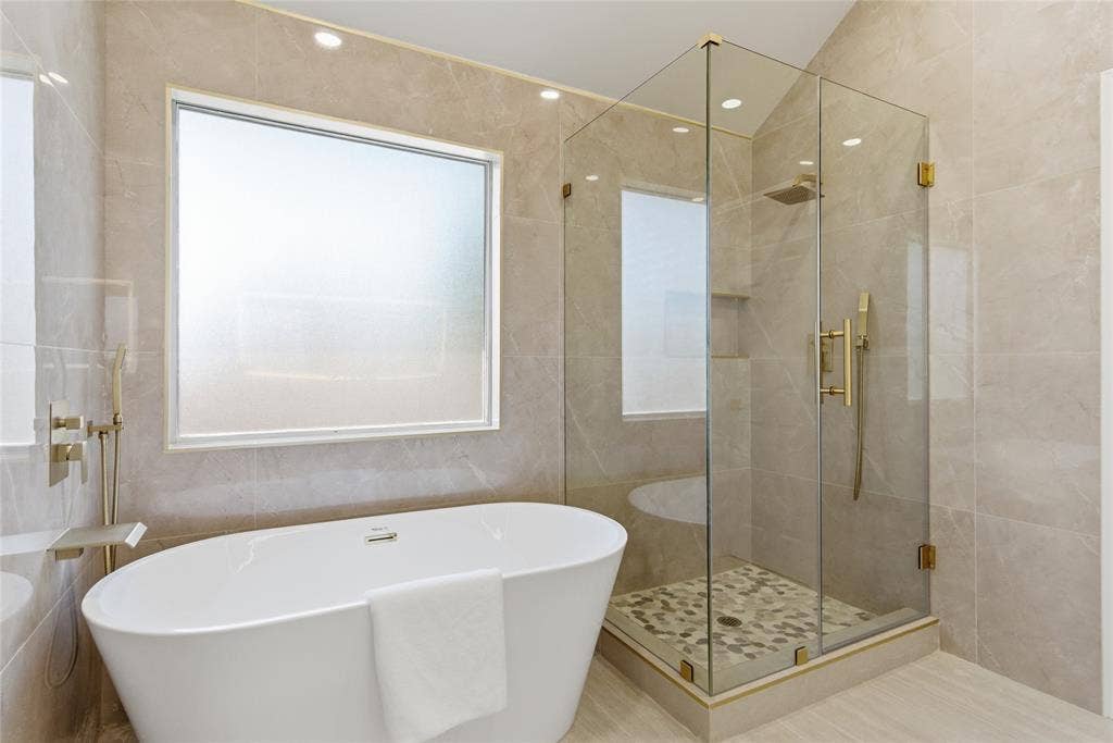 1416 Sunrise Lane, Sachse, TX 75048 Freestanding soaking tub with brushed brass fixtures, glass-enclosed shower with a mosaic tile floor, and large format wall tiling