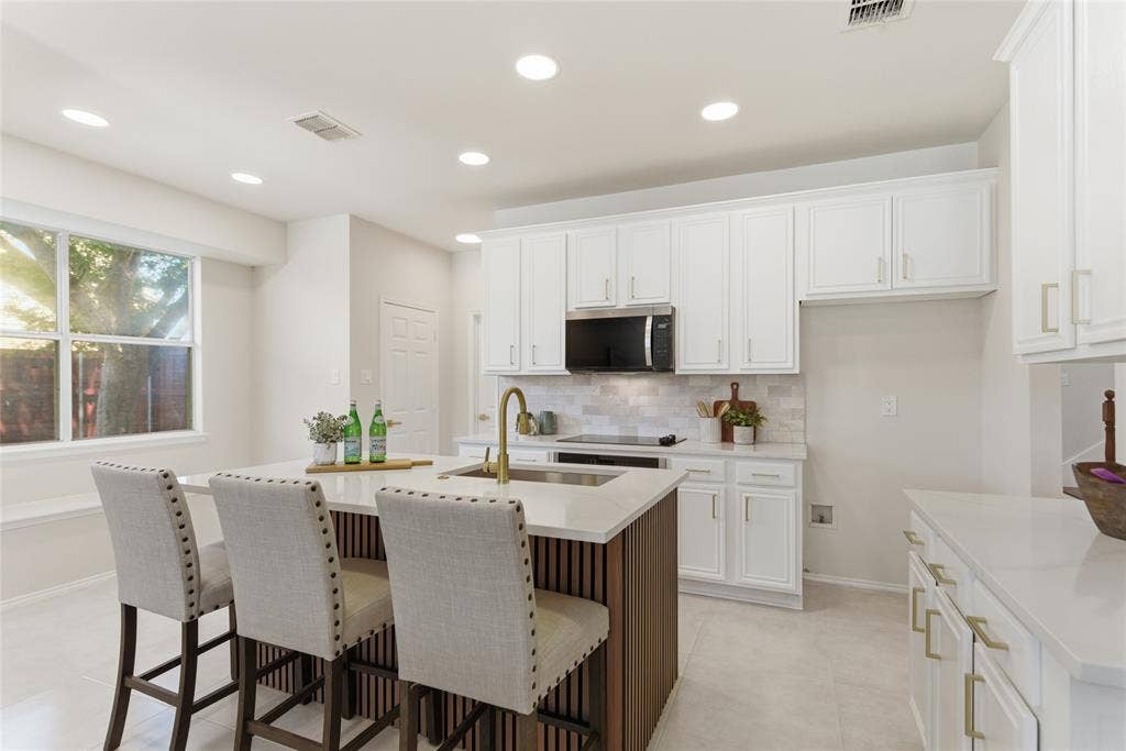 1416 Sunrise Lane, Sachse, TX 75048 White cabinetry with gold-tone hardware, a central island with a built-in sink and gold-tone faucet, a white tile backsplash, and recessed ceiling lighting