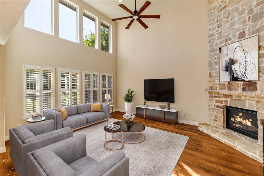 1049 Mesa Crest Drive, Fort Worth, TX 76052 Two-story living area featuring a stone-clad fireplace, elevated windows, wood-finish flooring, and a ceiling fan