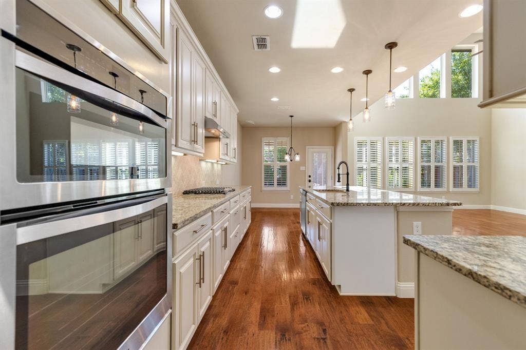 1049 Mesa Crest Drive, Fort Worth, TX 76052 Gourmet kitchen featuring stainless steel double ovens, a gas cooktop, granite countertops, wood-finish flooring, and white cabinetry with under-cabinet lighting