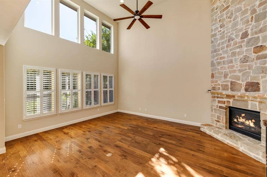 1049 Mesa Crest Drive, Fort Worth, TX 76052 Living room featuring hardwood flooring, stone-clad fireplace with hearth, vaulted ceiling, upper transom windows, and a ceiling fan