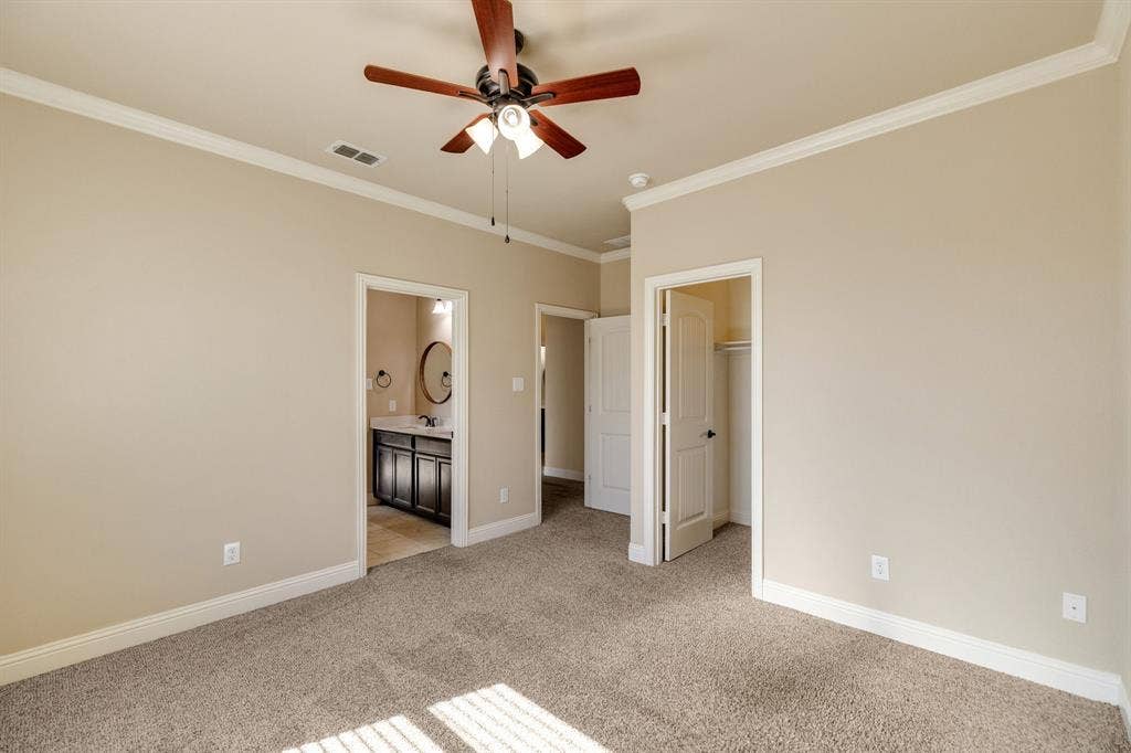 1049 Mesa Crest Drive, Fort Worth, TX 76052 Carpeted room featuring a ceiling fan, crown molding, and an attached bathroom with a dark wood-finish vanity and HUGE walk in closet