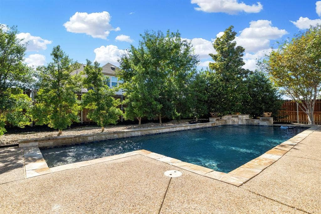 1049 Mesa Crest Drive, Fort Worth, TX 76052 Sparkling in-ground salt water pool with stone coping, surrounded by a textured concrete patio and mature upgraded landscaping
