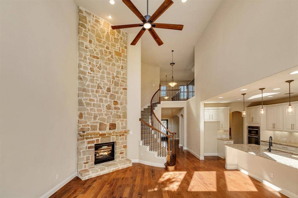 1049 Mesa Crest Drive, Fort Worth, TX 76052 Two-story stone fireplace with a modern insert, wood-finish flooring, a spiral staircase with wood and wrought iron railings, an open-concept kitchen with white cabinetry, and recessed lighting