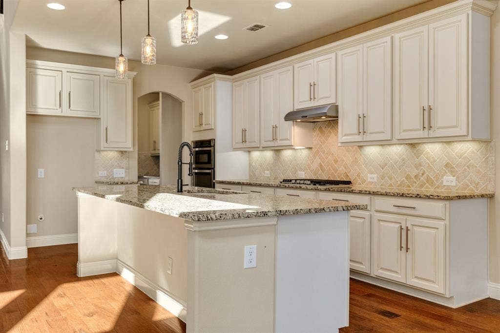 1049 Mesa Crest Drive, Fort Worth, TX 76052 Spacious kitchen featuring an island with breakfast area, light-toned cabinetry, herringbone tile backsplash, and wood-finish flooring