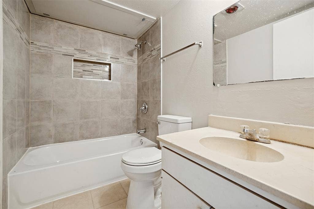11916 Leisure Drive, Dallas, TX 75243 Recessed shower niche with mosaic tile accent, tiled shower walls, built-in bathtub, chrome shower fixture, and vanity with integrated sink