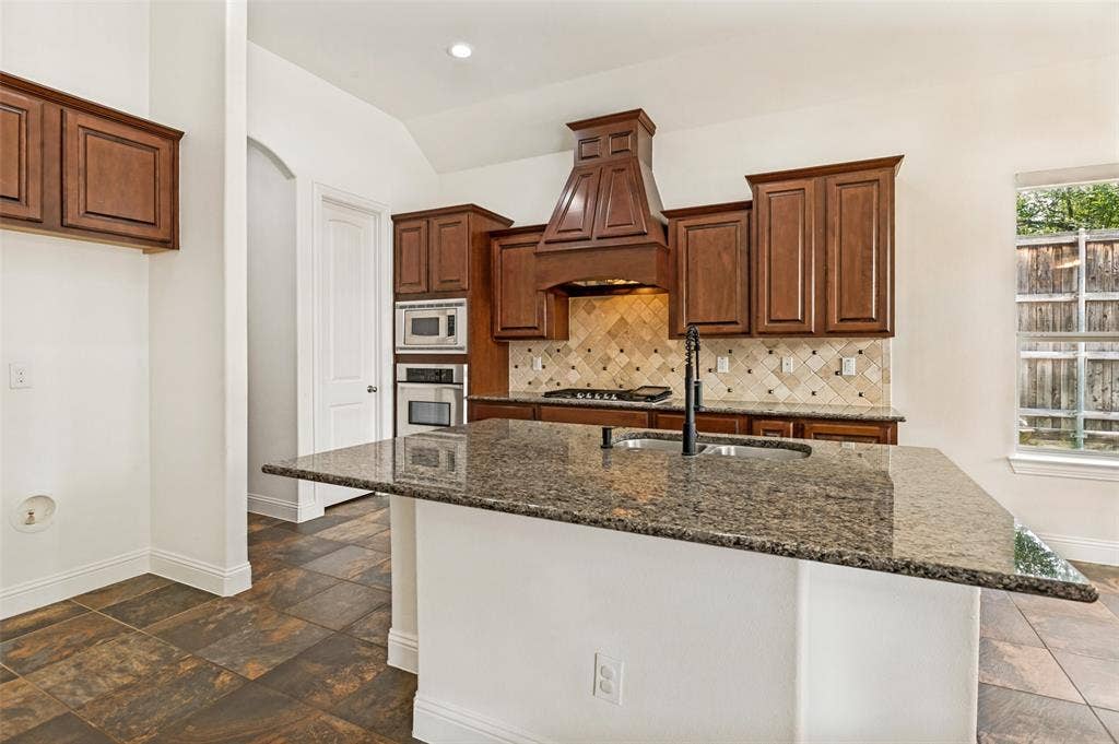 6734 Trailblazer Way, Dallas, TX 75236 Kitchen featuring a granite island, built-in stainless steel appliances, solid wood cabinetry, and a decorative tile backsplash