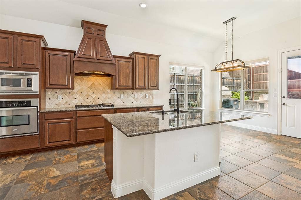 6734 Trailblazer Way, Dallas, TX 75236 Kitchen featuring rich wood cabinetry, stainless steel appliances, a center island with a sink, and patterned tile flooring