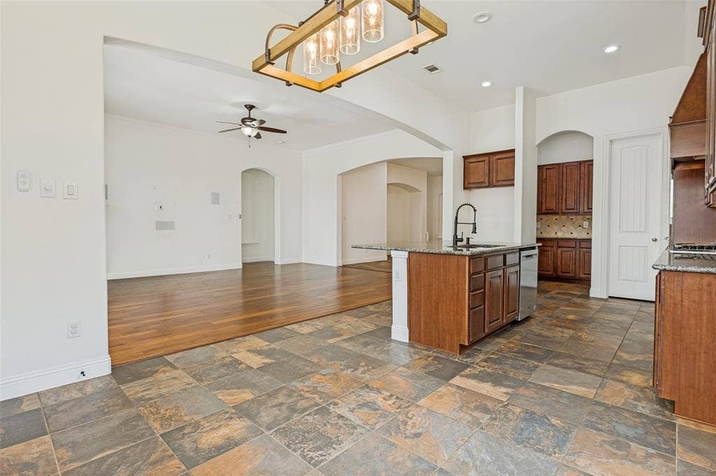 6734 Trailblazer Way, Dallas, TX 75236 Open-concept kitchen and dining area featuring slate-finish tile flooring, wood-finish cabinetry with contrasting island, stainless steel appliances, pendant lighting, and coffered ceiling with recessed lighting throughout