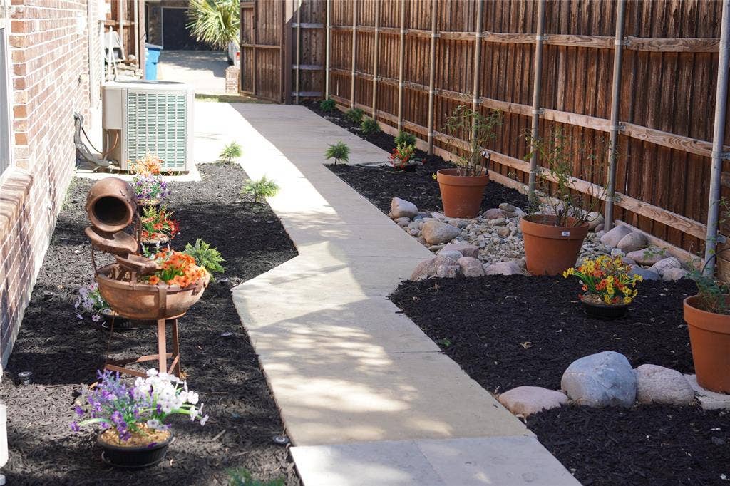 6734 Trailblazer Way, Dallas, TX 75236 Side yard featuring a concrete pathway, a wooden privacy fence, dark mulch beds, and decorative rocks