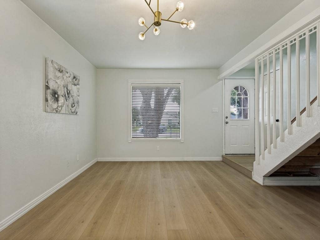 2018 Vail Drive, Garland, TX 75044 Wood-finish flooring throughout, modern chandelier, white staircase with vertical balusters, window with blinds, and an arched glass panel entry door