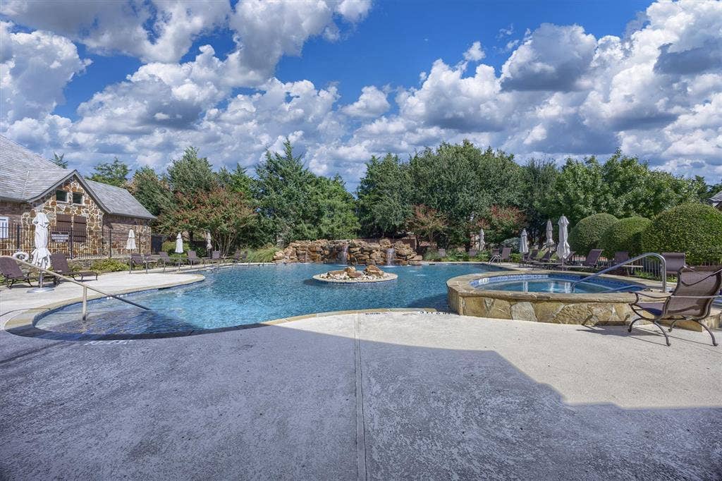 Large swimming pool with a stone waterfall feature, integrated spa, and surrounding hardscaping
