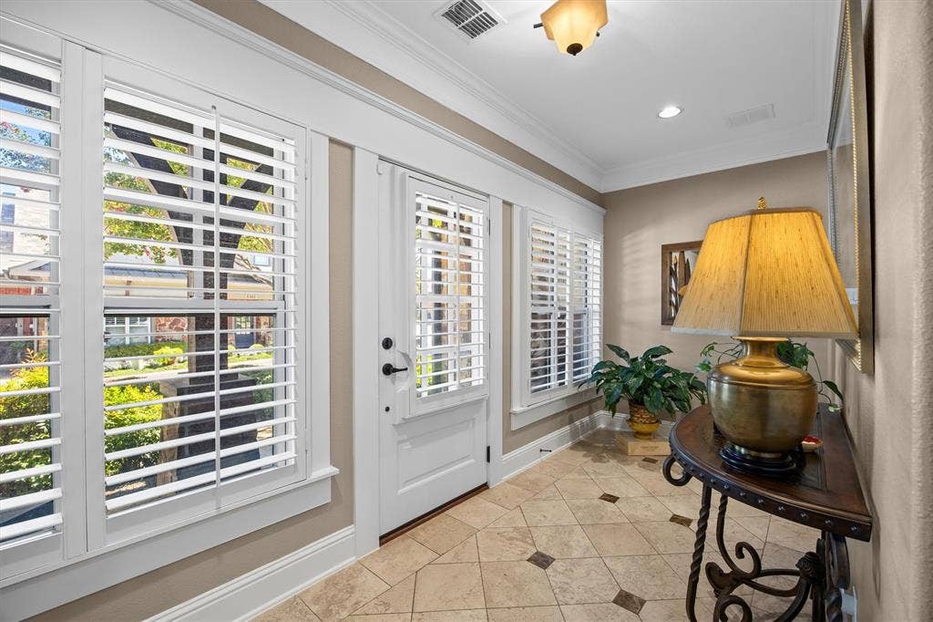 Entryway featuring tile flooring with decorative inserts, crisp white plantation shutters, crown molding, and a paneled door with matte black hardware.